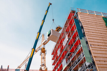 Crane lifting a wooden building module to its position in the structure. Construction site of an office building in Berlin. The new structure will be built in modular timber construction.