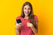 © luismolinero - Young woman using mobile phone isolated on yellow background with surprise facial expression