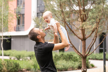 Wall Mural - Portrait of young handsome father holding his adorable cute newborn baby boy. Lifestyle. Real people. Fatherhood and parenthood concept. Happy father's day.