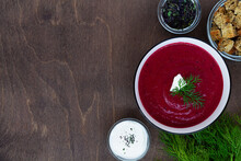 Red Beet Soup.vegetable Soup With Greens. Bowl Of Beetroot Cream Soup With Bread And White Cream On A Brown Wooden Background. Healthy Diet Lunch. Flat Lay, Top View. Copy Space