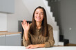 © Vadim Pastuh - Young and energetic asian female fresh graduate is ready for an online interview on a video call, sitting at the desk and looking and waving at the camera, saying hello. Job hunting concept