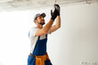 © Kostiantyn - Focused electrician in uniform installing light fitting in new apartment, standing on a ladder
