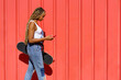 Black girl walking on an urban red background while consulting her smartphone.