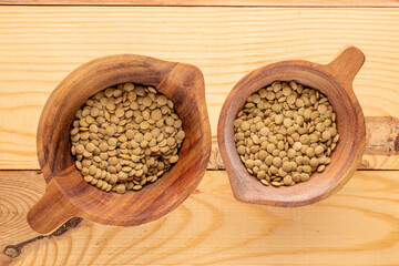 Uncooked organic green lentils in two wooden cups on a wooden table, macro, top view.