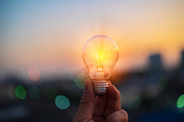 Wall Mural - man hands holds a house light bulb at sunset