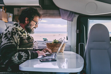 Wall Mural - Adult man use laptop computer to work inside camper van with roaming phone connection. Concept of modern people lifestyle in smart working or travel digital nomad freedom
