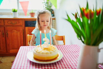 Wall Mural - Happy little girl celebrating her third birthday and making a wish