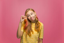 Cute Young Girl Look At Hand Showing With Fingers Something Small With Pity, Little Size Gesture On Pink Background