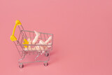 Fototapeta Mapy - Puppet hands pushing a trolley from a supermarket on a pink background, minimalism concept