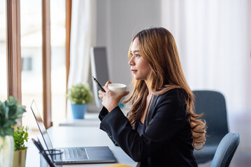 Wall Mural - Beautiful young Asian businesswoman drinking coffee working with laptop computer in office.