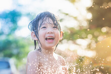 Asian Boy Has Fun Playing In Water From A Hose Outdoors