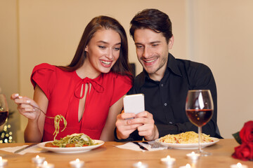 Smiling man and woman using mobile phone during dinner