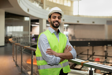 happy confident young attractive arabic engineer in hard hat and protective clothing in office plant