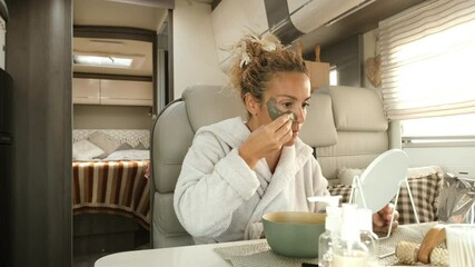 Wall Mural - Adult woman use facial cream aging treatment inside a camper van interior during travel holiday vacation. Care free body positive concept lifestyle with female people using mirror and creams