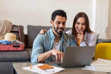 Young couple using laptop planning vacation and booking tickets online, preparing for vacation at home