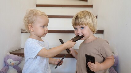 Two siblings sharing and feeding each other with chocolate bars enjoying childhood freedom and family fun