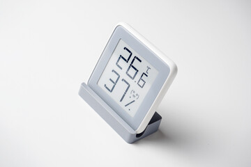 A home weather station standing on a white background is a modern device with a screen showing the temperature and humidity in the room. Side view