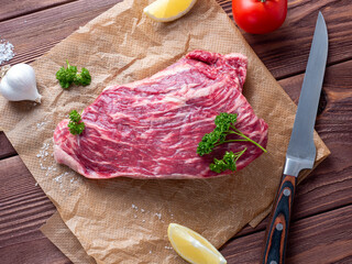 Canvas Print - A piece of fresh raw beef lies on parchment surrounded by spices, herbs and vegetables. The knife is lying nearby. Top view, flat lay. Food composition