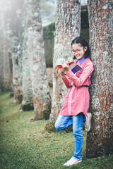 Poster - Smiling asian cute little girl with glasses reading book in park