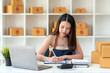 © amnaj - Online sales young Asian business owner woman is taking note of the customer's address on the parcel box being prepared for delivery.