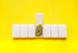 © Kemedo - White weekly pillbox with a big cannabis bud on yellow background with copy space. Concept of medical marijuana and CBD, natural medicines...