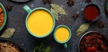 Healthy Indian Ayurveda Drink Mango Lassi In Two Cups On Rustic Concrete Table With Other Indian Food From Above, Yellow Blended Beverage Made Of Mango Fruit, Yoghurt Or Milk Curd And Spices 