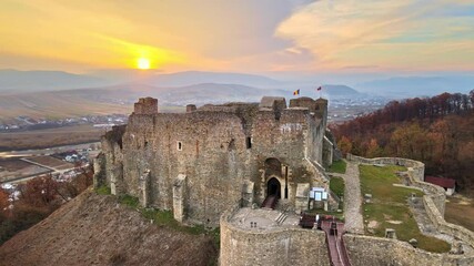 Wall Mural - Aerial drone view of the Neamt Citadel in Targu Neamt, Romania. Fortress on the top of a hill, surrounded by lush yellowed forest, tourists, town on the background