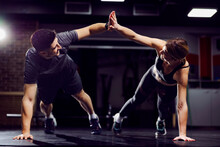 A Fit Sporty Couple Giving High Five To Each Other While Doing Planks And Exercises In A Gym.