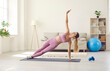 © Studio Romantic - Fit woman having fitness workout at home. Slim young Caucasian lady in modern light mauve or pale purple pink color sports bra top and leggings doing side plank exercise on rubber mat in living room