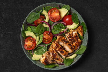 Wall Mural - Grilled chicken breast and spinach salad with avocado, tomatoes and sesame seeds in a plate on dark background