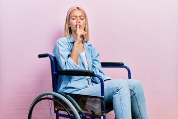 Poster - Beautiful blonde woman sitting on wheelchair asking to be quiet with finger on lips. silence and secret concept.