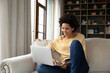 © fizkes - Happy beautiful millennial African American woman using computer, reading message with good news, watching funny movie, communicating in social network, shopping online or working distantly at home.