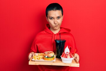 Poster - Beautiful hispanic woman with short hair eating a tasty classic burger with fries and soda skeptic and nervous, frowning upset because of problem. negative person.