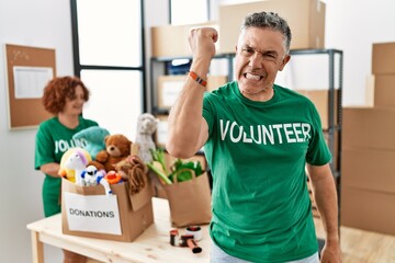 Wall Mural - Middle age man wearing volunteer t shirt at donations stand angry and mad raising fist frustrated and furious while shouting with anger. rage and aggressive concept.