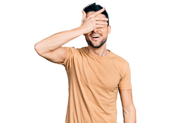 Poster - Hispanic man with beard wearing casual t shirt smiling and laughing with hand on face covering eyes for surprise. blind concept.