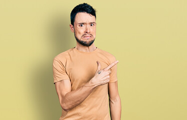 Hispanic man with beard wearing casual t shirt pointing aside worried and nervous with forefinger, concerned and surprised expression