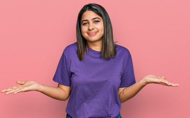 Sticker - Young hispanic girl wearing casual purple t shirt clueless and confused expression with arms and hands raised. doubt concept.