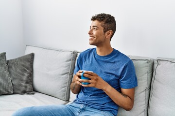 Poster - Young hispanic man relaxing sitting on the sofa drinking a coffee at home