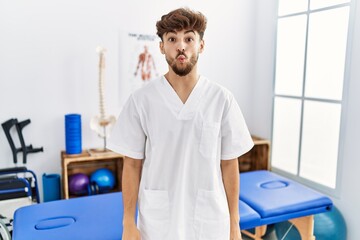 Sticker - Young arab man working at pain recovery clinic making fish face with lips, crazy and comical gesture. funny expression.