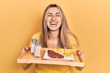 Poster - Beautiful hispanic woman holding tray with lunch smiling and laughing hard out loud because funny crazy joke.