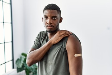 Sticker - Young african american man getting vaccine showing arm with band aid thinking attitude and sober expression looking self confident