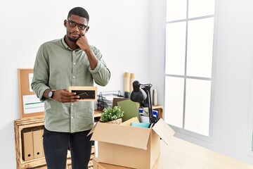 Canvas Print - Young african american businessman unboxing box at the office with hand on chin thinking about question, pensive expression. smiling with thoughtful face. doubt concept.