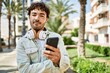 © Krakenimages.com - Handsome hispanic man with beard smiling happy outdoors on a sunny day wearing headphones listening to music with smartphone