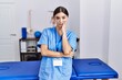 © Krakenimages.com - Young hispanic woman wearing physiotherapist uniform standing at clinic thinking looking tired and bored with depression problems with crossed arms.