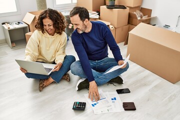 Poster - Middle age hispanic couple smiling happy controlling family economy. Sitting on the floor at new home.