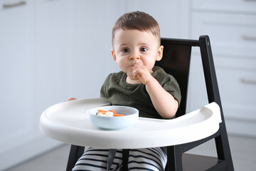 Poster - Cute little baby eating healthy food in high chair at home