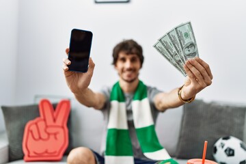 Sticker - Young hispanic man holding smartphone and dollars at home