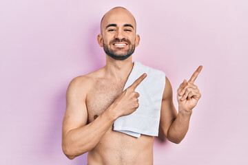 Canvas Print - Young bald man standing shirtless smiling and looking at the camera pointing with two hands and fingers to the side.