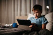 © OlgaKhorkova - Little boy using tablet while laying in bed in living room.