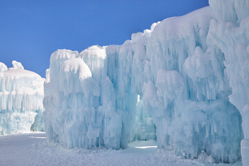 Wall Mural - Clear blue sky on a winter day with huge icicles dripping on a giant frozen snow fort